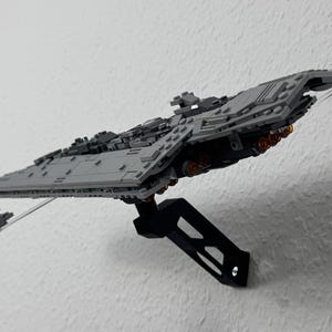 May include: A grey model of a Star Destroyer spaceship, mounted on a black stand. The model has detailed features, including multiple turrets and engine details. The spaceship is angled, giving a sense of flight.