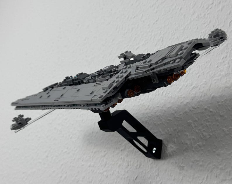 May include: A grey model of a Star Destroyer spaceship, mounted on a black stand. The model has detailed features, including multiple turrets and engine details. The spaceship is angled, giving a sense of flight.