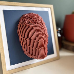 May include: A framed 3D wall art piece featuring a red, textured, abstract design. The artwork is displayed against a dark blue background.