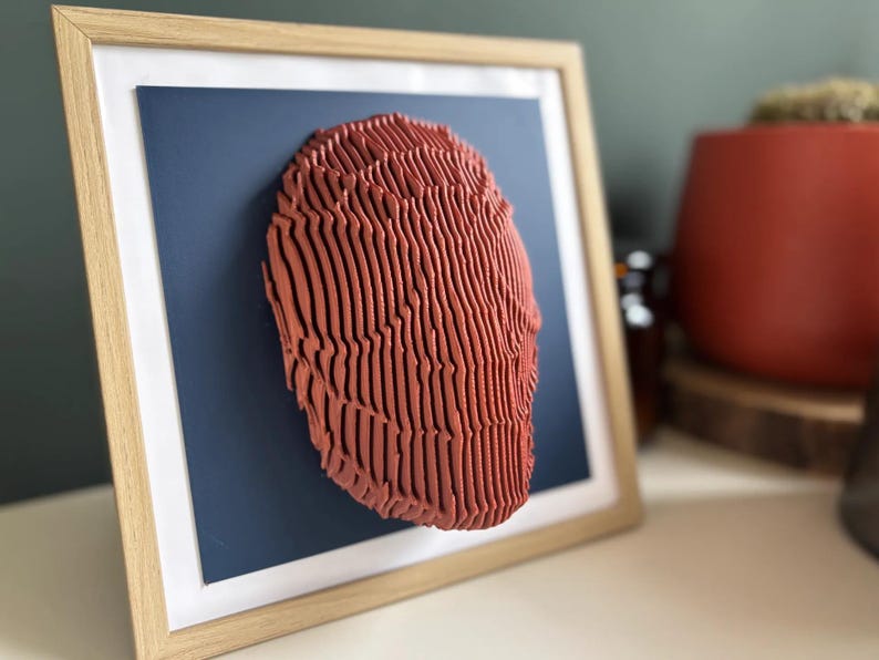 May include: A framed 3D wall art piece featuring a red, textured, abstract design. The artwork is displayed against a dark blue background.