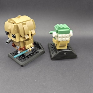 Może przedstawiać: Dwie minifigurki Lego, jedna przedstawiająca Yodę, a druga Jedi, są wystawione na czarnych podstawkach Lego. Figurki są zwr&oacute;cone do siebie.