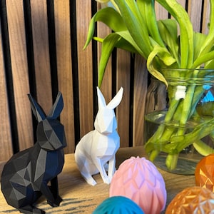 May include: A white and a black geometric bunny figurine, along with four geometric Easter eggs in pink, blue, and orange.