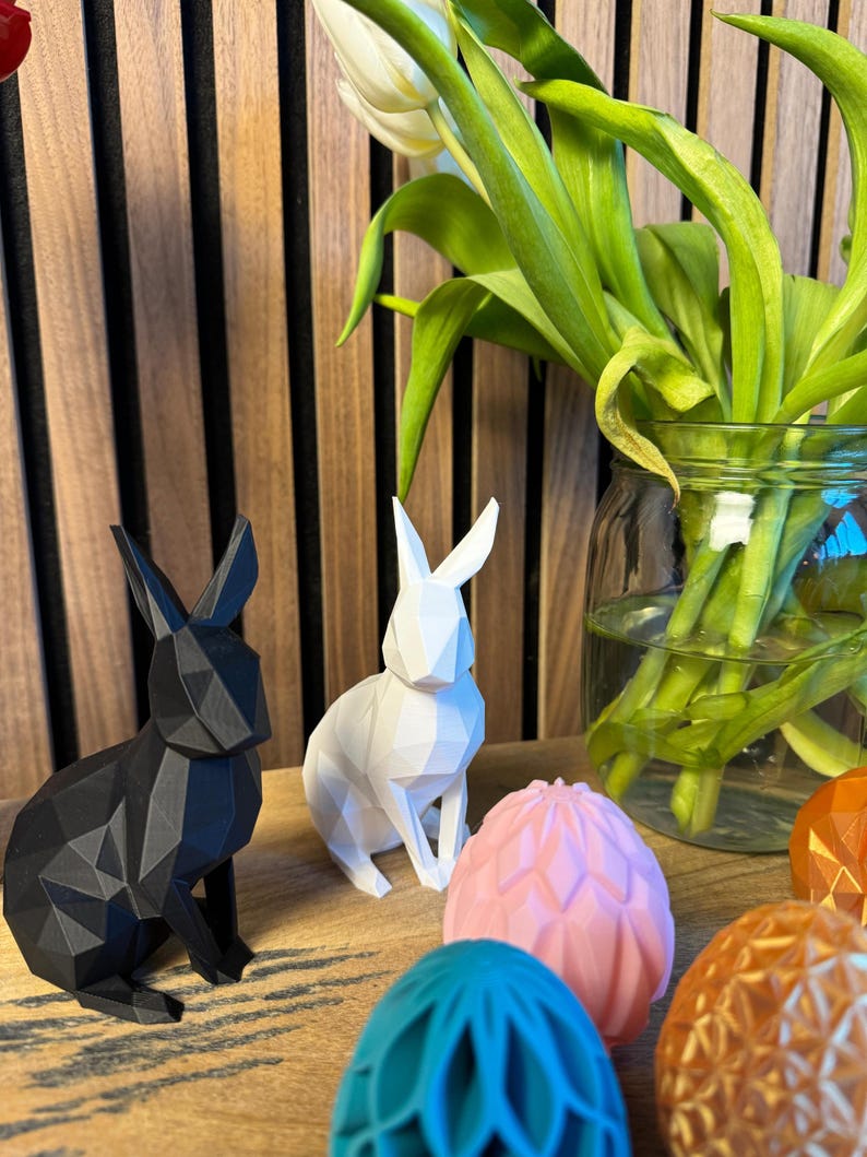 May include: A white and a black geometric bunny figurine, along with four geometric Easter eggs in pink, blue, and orange.