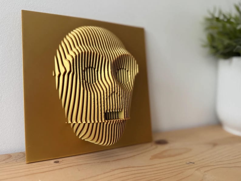 Puede incluir: Una escultura abstracta de rostro en 3D impresa en oro, montada sobre un fondo dorado.