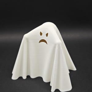Puede incluir: Figurita de fantasma blanco con una cara fruncida, hecha de pl&aacute;stico impreso en 3D.