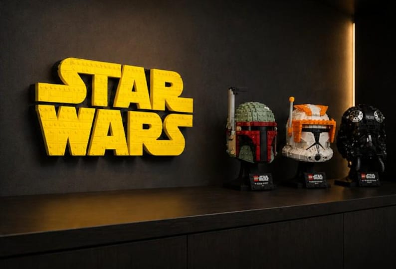 Pode incluir: Letreiro amarelo LEGO "STAR WARS" em uma parede preta. Tr&ecirc;s capacetes LEGO s&atilde;o exibidos em uma prateleira abaixo do letreiro. Os capacetes s&atilde;o Boba Fett, um Clone Trooper e um piloto imperial preto.