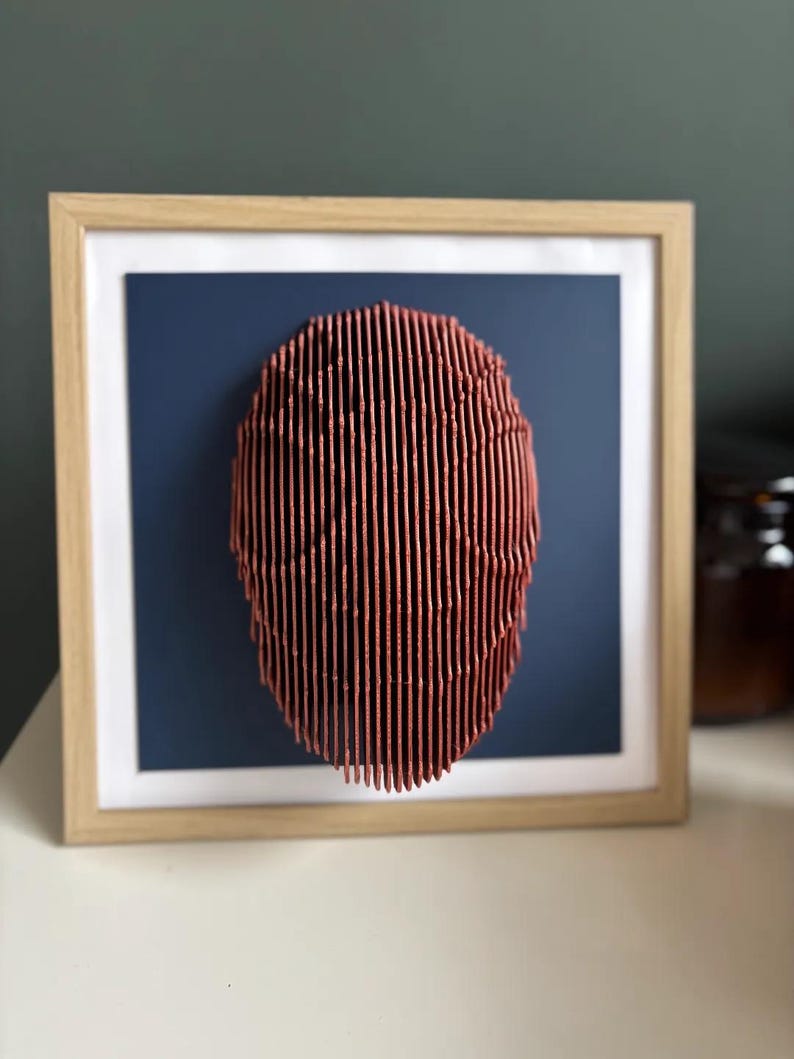 May include: A framed wall art piece featuring a 3D abstract sculpture made of thin, vertical, red lines. The sculpture is circular and appears to be made of wood. The sculpture is mounted on a dark blue background.