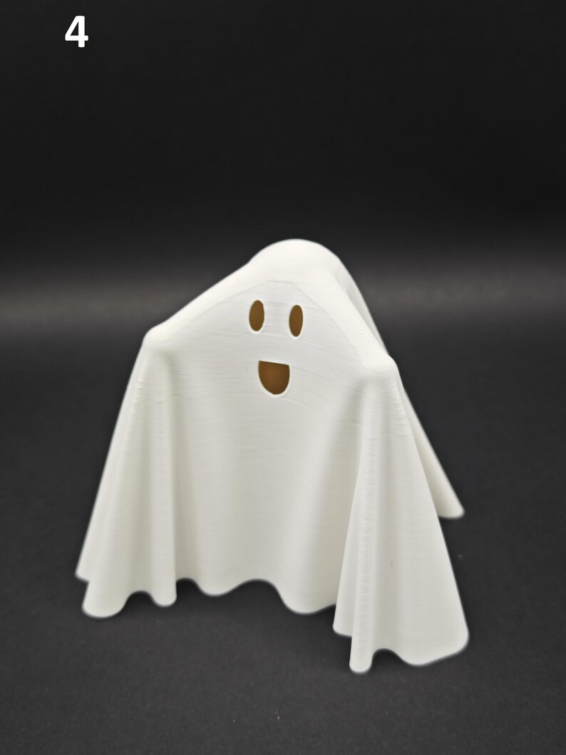 Puede incluir: Figurita de fantasma blanco con una cara sonriente. El fantasma est&aacute; hecho de un material blanco liso y tiene una forma fluida y drapeada.