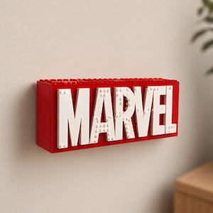 May include: A red and white Marvel logo constructed from interlocking toy bricks. The word "MARVEL" is spelled out in large white letters against a red background. The logo is mounted on a white wall.