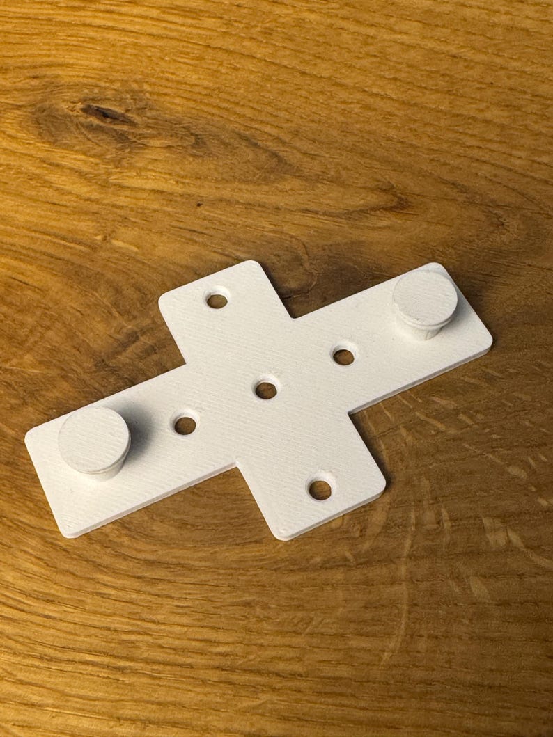 May include: White plastic cross-shaped bracket with five holes and two round knobs.
