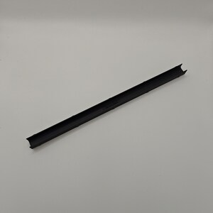 May include: A long, black plastic strip with a channel down the middle. The ends are notched. The object is on a white background.