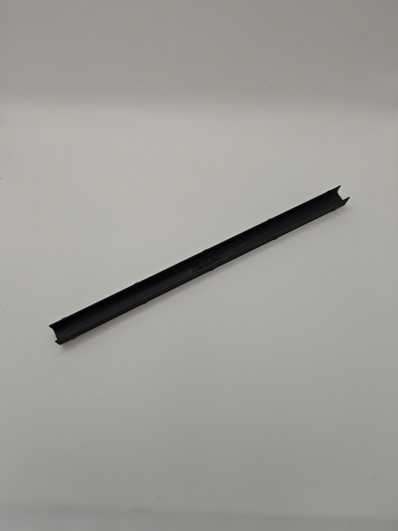 May include: A long, black plastic strip with a channel down the middle. The ends are notched. The object is on a white background.