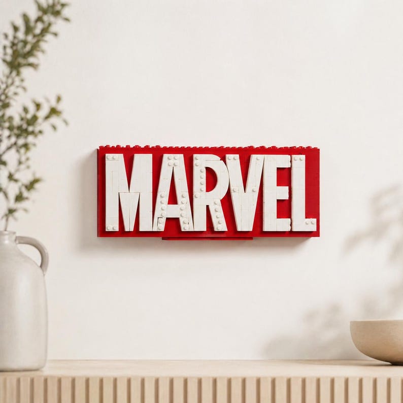 May include: A red and white Marvel logo made of interlocking blocks. The word "MARVEL" is spelled out in white letters against a red background. The logo is mounted on a white wall.