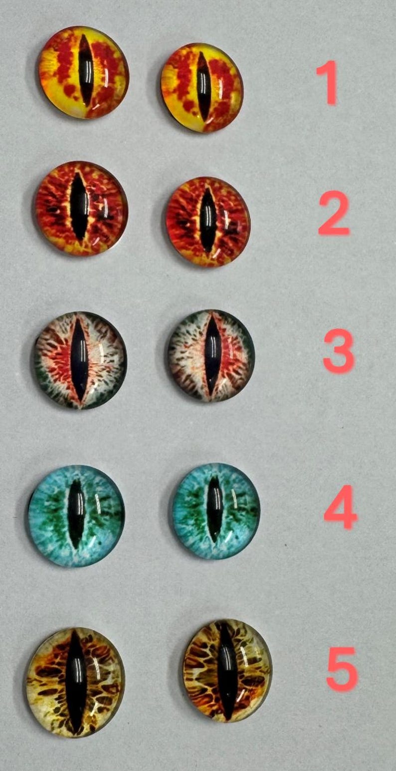May include: A collection of ten glass eye cabochons in various colors. The eyes are round with a black slit pupil and detailed iris patterns in shades of yellow, red, white, and blue. Each eye is numbered 1 through 5.