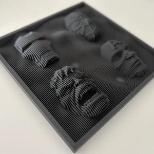 May include: A black framed wall art piece with four 3D printed faces. The faces are stylized and have a textured, layered look.