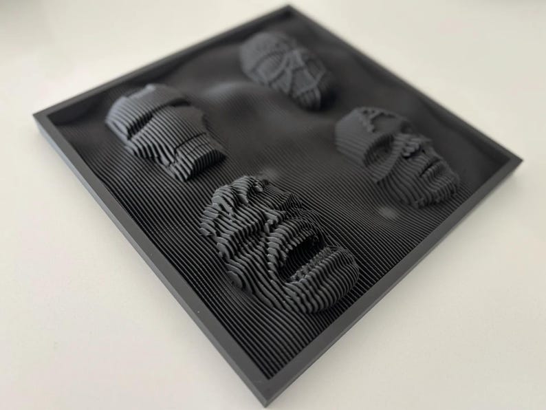 May include: A black framed wall art piece with four 3D printed faces. The faces are stylized and have a textured, layered look.