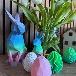 May include: A set of colorful geometric Easter decorations, including a blue and green bunny, a pink egg, a white egg with a textured surface, a green egg with a wavy surface, and a green and white egg with a geometric pattern.