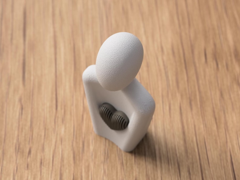 May include: A white abstract sculpture with a textured egg-shaped head and a dark gray heart-shaped element in the chest. The sculpture is set against a wooden background.