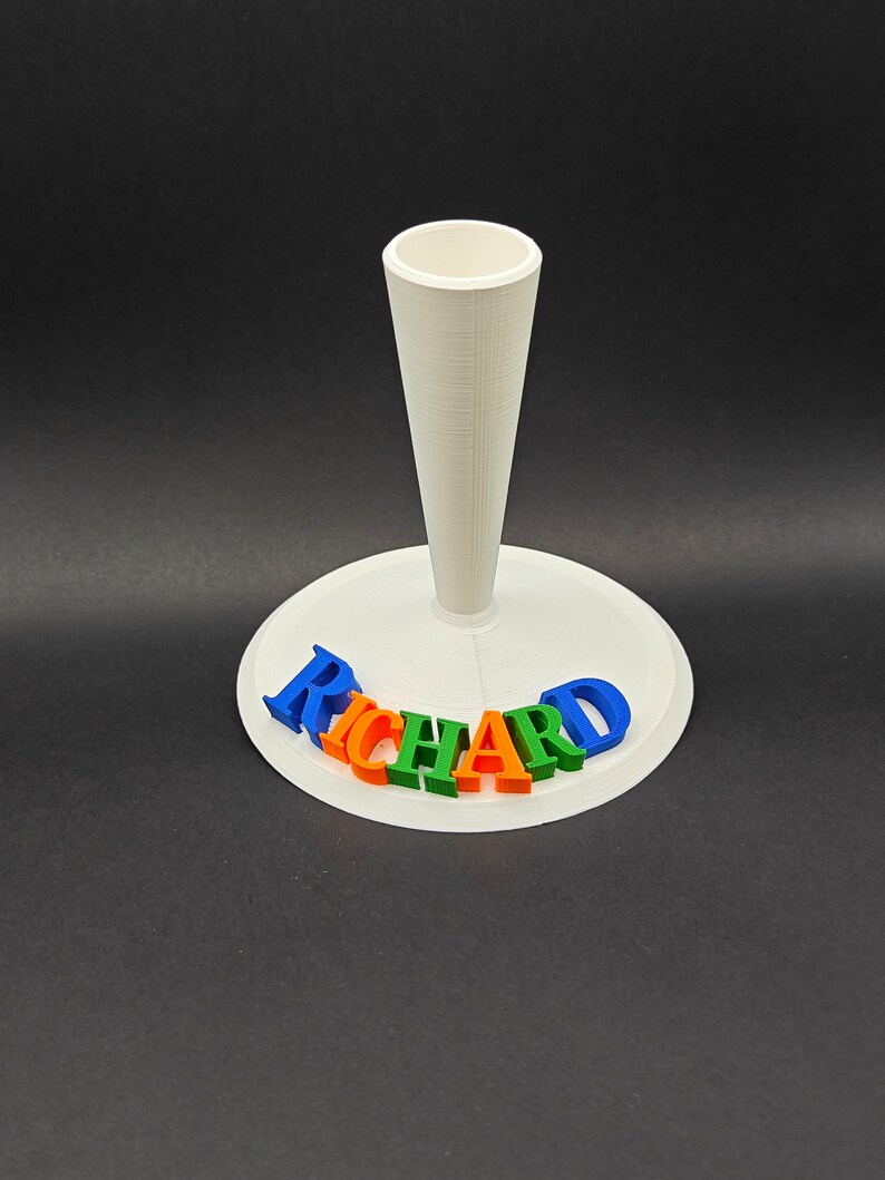 Puede incluir: Soporte blanco impreso en 3D con un soporte en forma de cono y el nombre "RICHARD" escrito en letras azules, verdes, naranjas y rojas.
