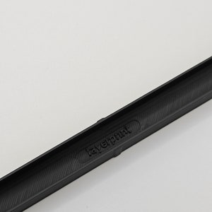 May include: A black, rectangular object with the text "layerprint" embossed on its surface. The object has a textured interior and is set against a white background. The item appears to be a component or part of a larger product.