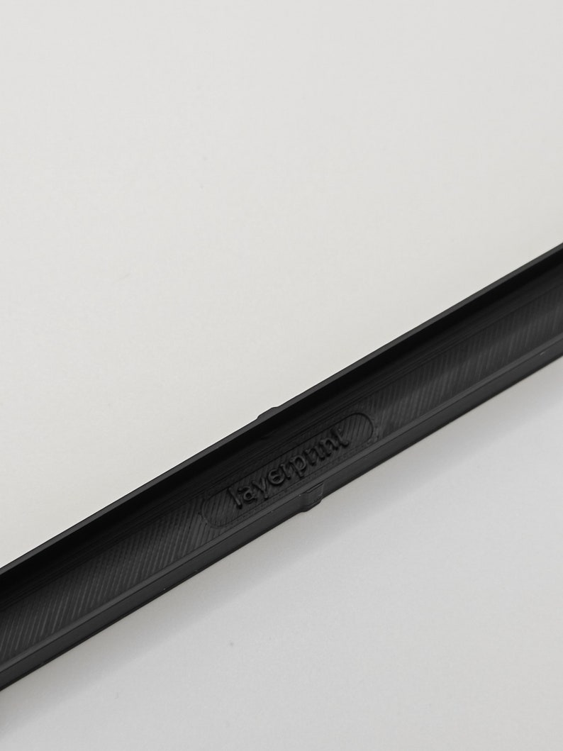 May include: A black, rectangular object with the text "layerprint" embossed on its surface. The object has a textured interior and is set against a white background. The item appears to be a component or part of a larger product.