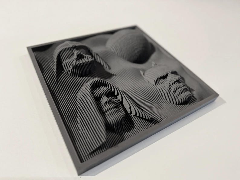 May include: A gray framed wall art piece with a 3D design of four faces. The faces are made of layered lines and appear to be from a science fiction movie.
