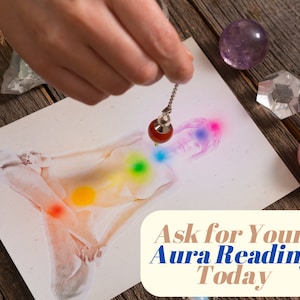 May include: A white card with a drawing of a person sitting in a meditative pose with seven colorful chakras. A hand holds a pendulum over the drawing. The card has the text "Ask for Your Aura Reading Today".
