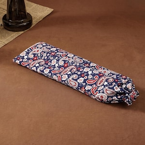 Puede incluir: Una bolsa de tela rectangular con fondo azul oscuro y un patr&oacute;n repetitivo de remolinos de cachemira blancos y rojos junto a peque&ntilde;os motivos florales. La bolsa tiene un extremo fruncido con cierre de cord&oacute;n, creando una forma cil&iacute;ndrica suave.