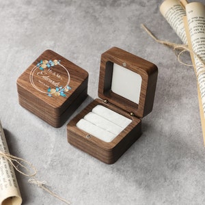 Könnte beinhalten: Eine Holzkiste für Ringe mit einem Blumendesign und dem Text "Mr. & Mrs. Edwards" sowie dem Datum "March 12, 2023". Die Kiste hat einen Klappdeckel und ein Samt-Innenfutter mit drei Ringfächern.