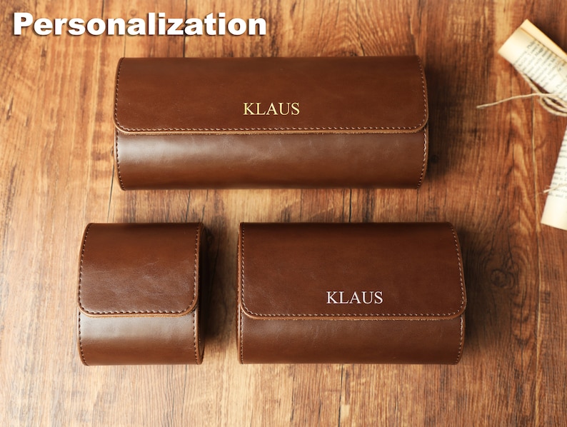 K&ouml;nnte beinhalten: Drei braune Lederuhrenboxen mit dem Namen "KLAUS" in goldenen Lettern gepr&auml;gt. Die Boxen sind in verschiedenen Gr&ouml;&szlig;en und auf einer Holzoberfl&auml;che angeordnet.