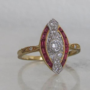Puede incluir: Un anillo de oro con un diamante central rodeado por un anillo de rubíes rojos y diamantes más pequeños.