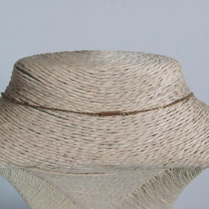 May include: A delicate gold-colored necklace displayed on a mannequin. The necklace features a fine chain with a small rectangular bar at the back. The mannequin is covered in a woven, beige material, set against a light blue background.