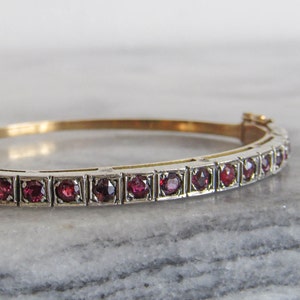 Pode incluir: Um bracelete de ouro com uma fila de pedras preciosas vermelhas engastadas em prata.