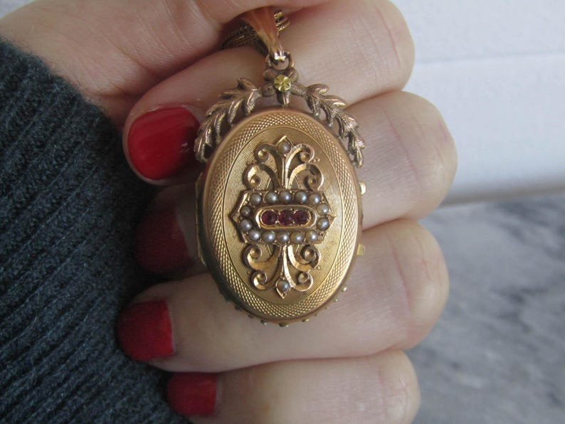 May include: A gold locket with a delicate floral design and a red and white stone accent. The locket is open and has a small mirror inside.