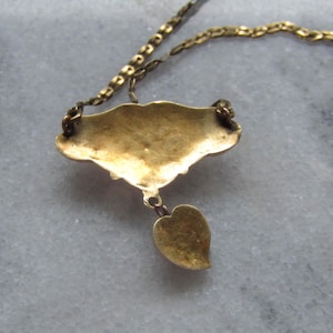May include: A gold-toned necklace with a pendant featuring a stylized leaf and a decorative, fan-shaped element. The chain and pendant have a vintage appearance, suggesting an antique or vintage jewelry piece.