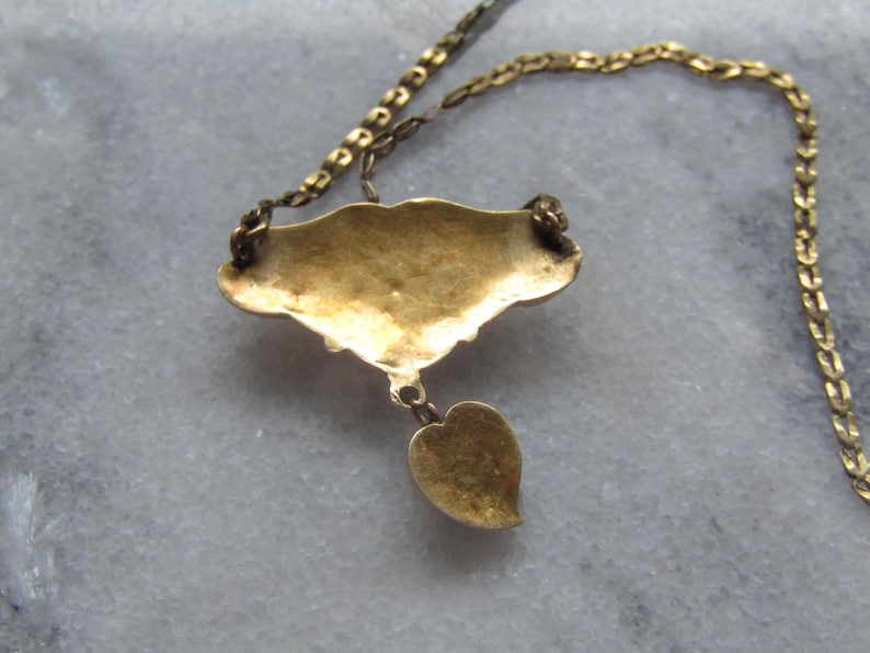 May include: A gold-toned necklace with a pendant featuring a stylized leaf and a decorative, fan-shaped element. The chain and pendant have a vintage appearance, suggesting an antique or vintage jewelry piece.