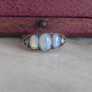 May include: A gold ring with four oval-shaped opals set in a row. The opals are a pale blue color with a slight iridescent sheen.
