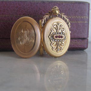 May include: Gold locket with an engraved monogram and a floral design. The locket is decorated with pearls and red gemstones.