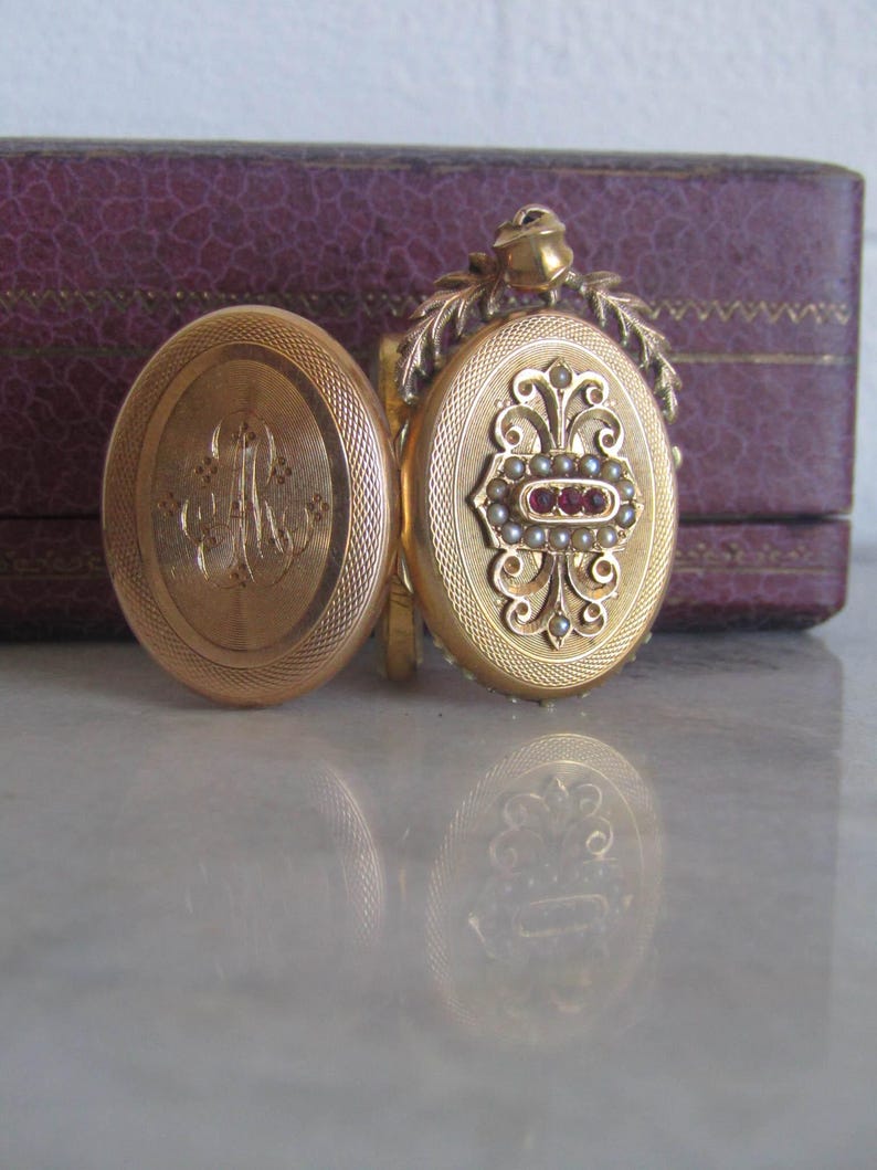 May include: Gold locket with an engraved monogram and a floral design. The locket is decorated with pearls and red gemstones.