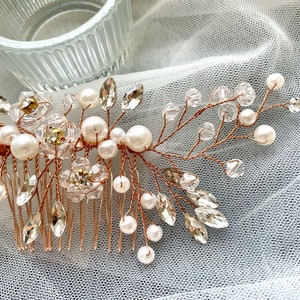 May include: A rose gold hair comb with a delicate design featuring clear and gold crystals, pearls, and wire branches. The comb is perfect for adding a touch of sparkle to any hairstyle.