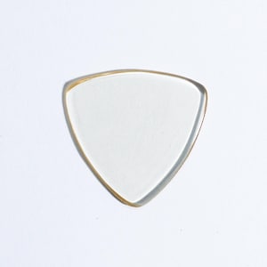 Puede incluir: Una púa de guitarra triangular transparente con un borde dorado.