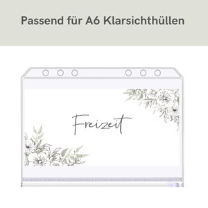 May include: A clear plastic A6 envelope with a white background and a floral design. The text "Freizeit" is written in black cursive on the envelope.
