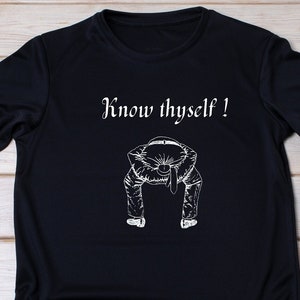 Può includere: Maglietta nera con una grafica bianca di una persona che si piega con il testo "Know thyself!" stampato sul davanti.