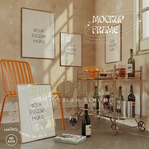 Può includere: Un carrello bar in metallo dorato con due ripiani e ruote. Il carrello è pieno di bottiglie di vino e liquore, bicchieri e un secchiello per il ghiaccio argentato. Ci sono tre quadri incorniciati sul muro dietro il carrello. I quadri sono tutti vuoti e hanno il testo "YOUR DESIGN HERE" scritto su di essi. Il carrello è in una stanza con una parete marrone e un pavimento in legno. C'è una sedia in primo piano dell'immagine.