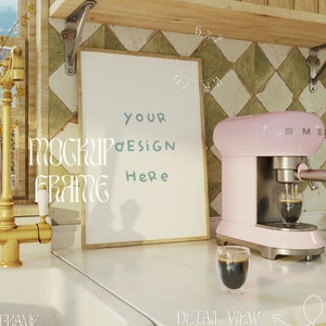 Può includere: Un mockup di cornice bianca con il testo "YOUR DESIGN HERE" su un bancone da cucina con una macchina per espresso rosa e un bicchiere di caffè.