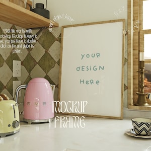 Puede incluir: Una maqueta de marco de imagen blanco con un marco de madera, sentado en una encimera blanca en un entorno de cocina. El marco está vacío y listo para su diseño. El texto "YOUR DESIGN HERE" está escrito en el marco.