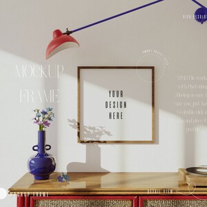 May include: A wooden frame mockup with a light brown frame and a white background. The text "YOUR DESIGN HERE" is visible in the frame. The frame is on a wooden table with a blue vase with flowers and a record player.