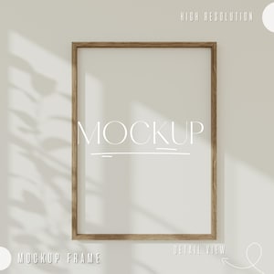 Könnte beinhalten: Ein Holzrahmen-Mockup mit weißem Hintergrund. Der Rahmen befindet sich an einer weißen Wand mit einem Schatten von einem Fenster. Der Text "MOCKUP" ist in Weiß auf dem Rahmen geschrieben.