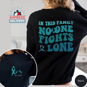 May include: Black sweatshirt with the text "In this family no one fights alone" in teal and blue lettering. A teal ribbon is below the text. The sweatshirt has a teal ribbon on the front with the text "Team Emily".
