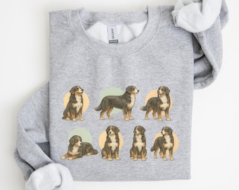 Puede incluir: Sudadera gris claro con un patrón repetido de perros de montaña berneses en varias poses. Cada ilustración de perro está colocada sobre un círculo verde claro o amarillo verdoso. Los perros están representados en tonos de marrón, negro y blanco.
